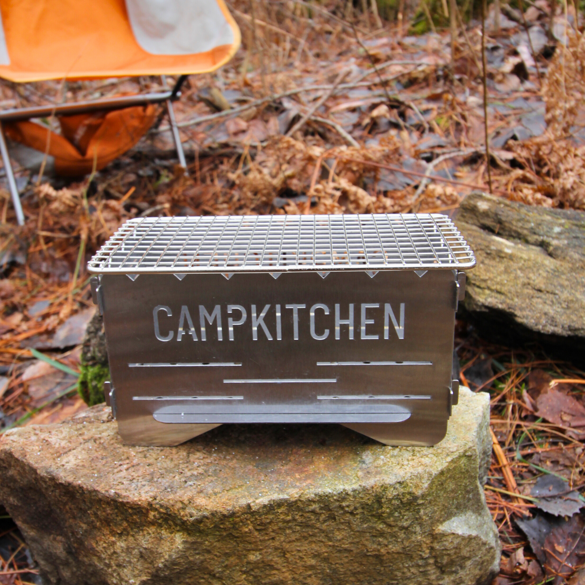 CAMPKITCHEN Twig Stove complete with grate top resting on a large rock.