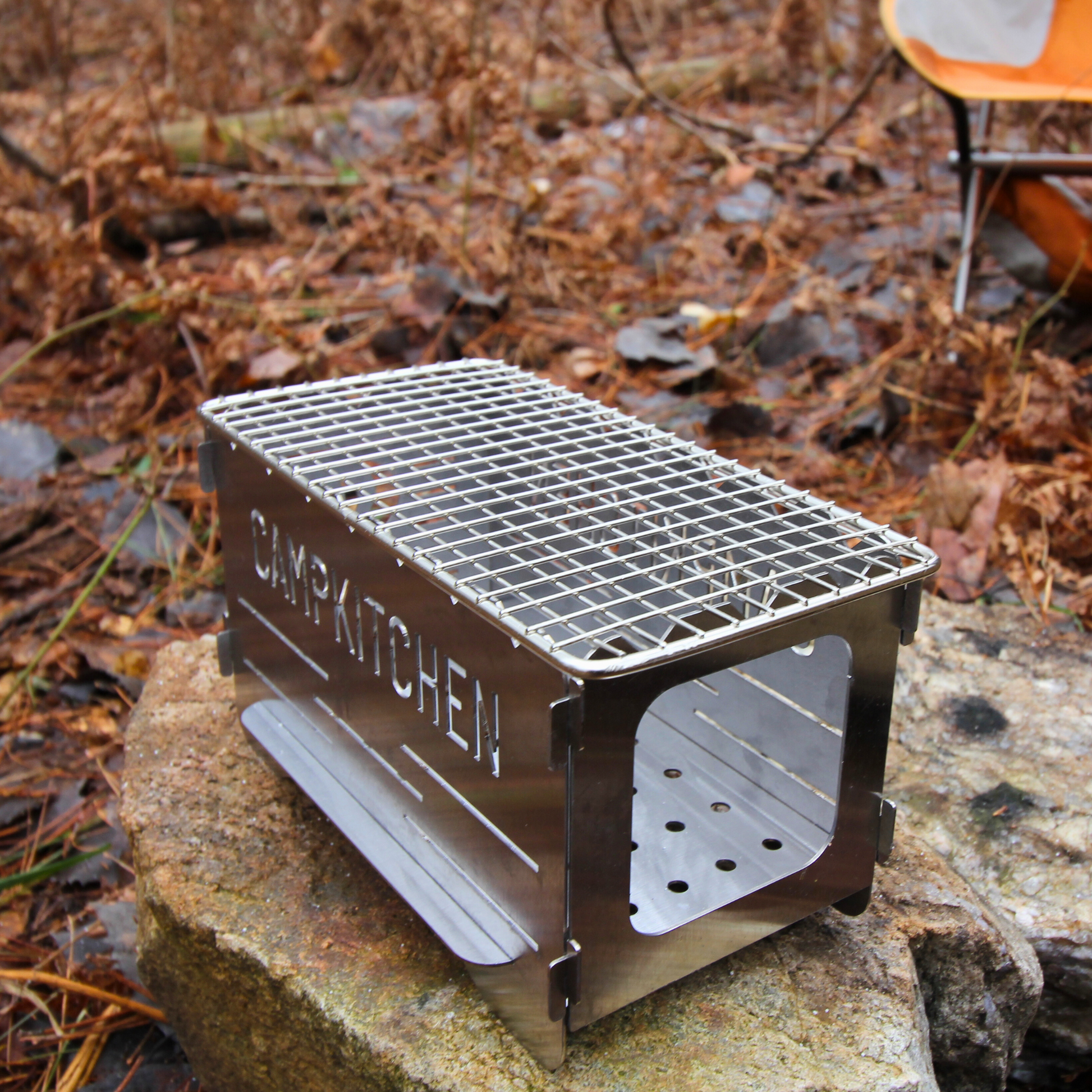 CAMPKITCHEN Twig Stove. Stove is on an angle showcasing an open end which is used to fuel the fire with twigs and small pieces of wood.